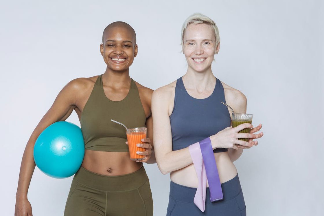 Two women in their athleisure both holding pre workout smoothies in a glass and steel straws