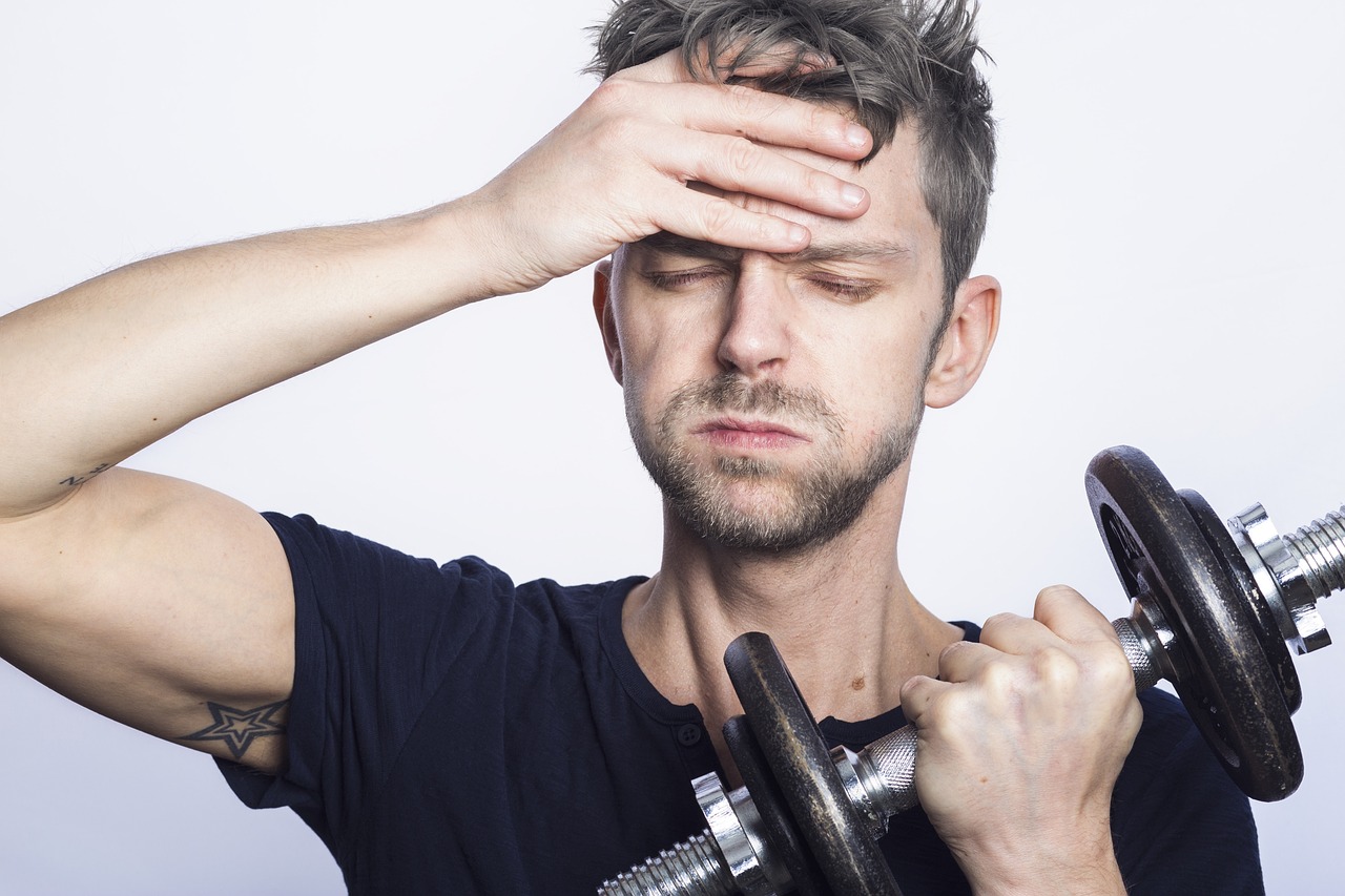 A man wearing a black shirt is holding a black and silver dumbbell near a white wall