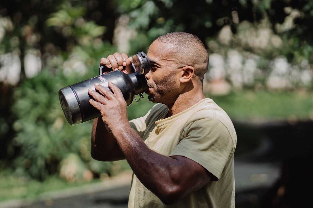 A man wearing a yellow shirt is holding a black water bottle with a black lid