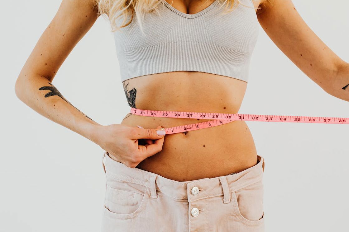 Woman wearing loose jeans measuring her waist with a pink tape measure