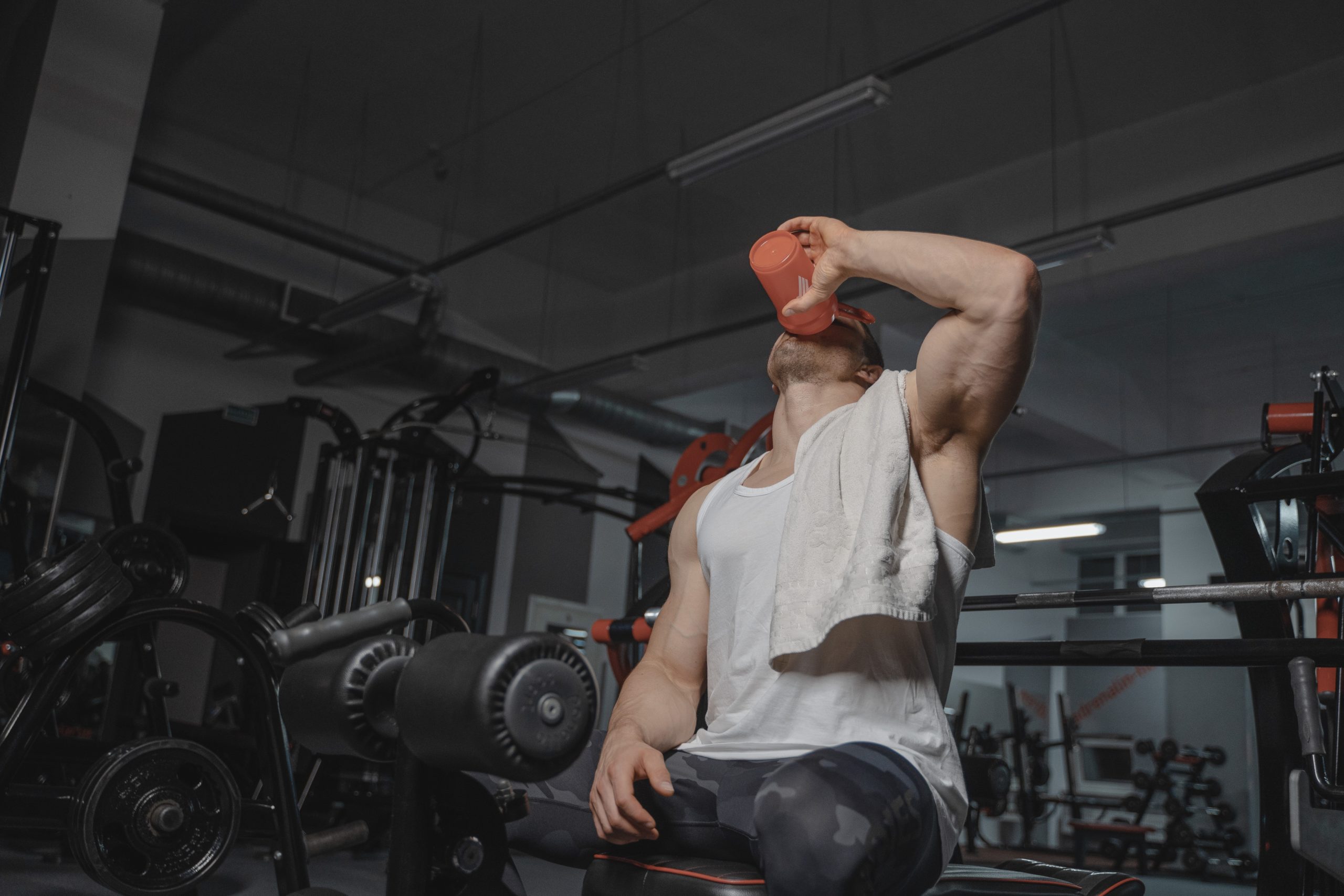 A man on the gym sitting while drinking on an orange tumbler