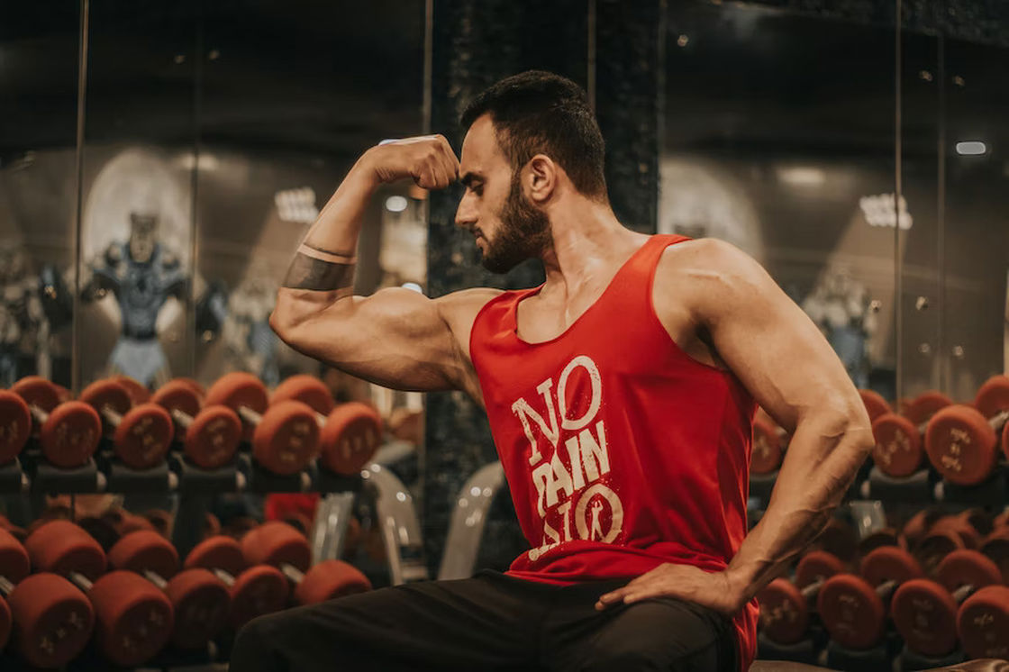 Man flexing his biceps while sitting down on a bench inside the gym