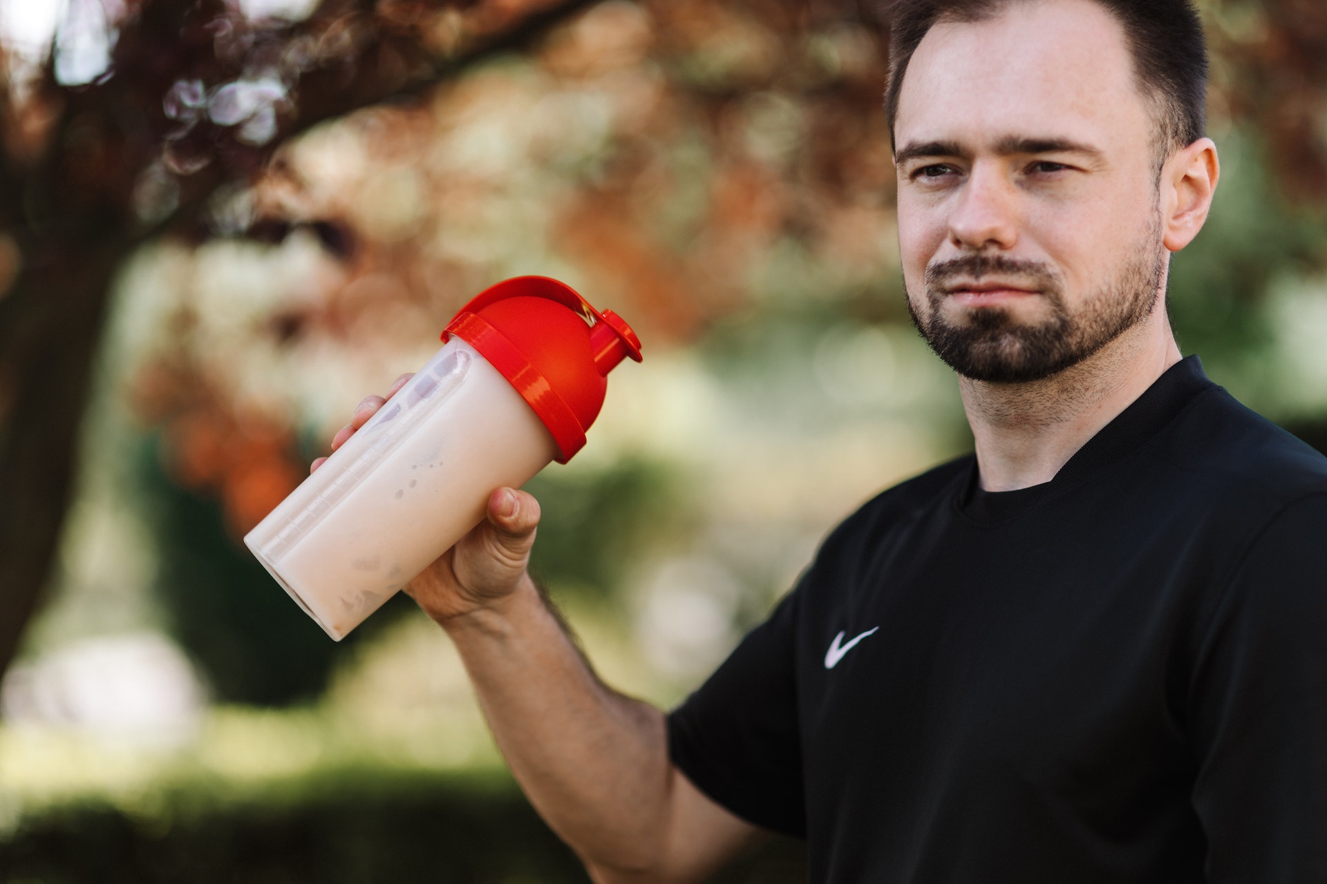 A man wearing black shirt is shaking a plastic tumbler with red lid