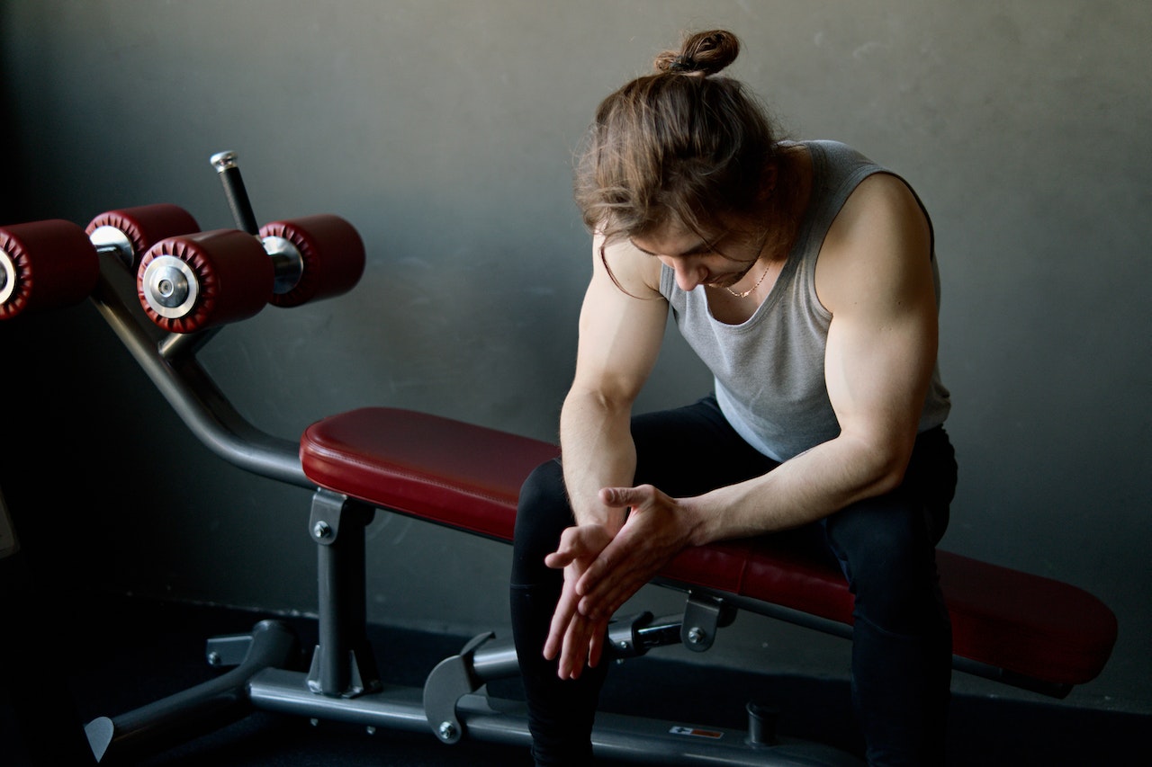 A person wearing a gray tank top and black leggings is sitting on a black and red gym equipment